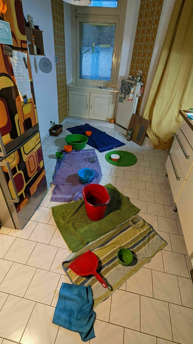 Töpfe und Wannen und Tücher auf dem Boden: Fehlende Dachwasserableitung führt in der Wohnung zu Wassereinbrüchen