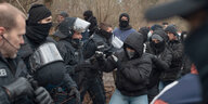 Polizisten, teils vermummt und mit Helmen, rangeln mit mehreren Menschen mit schwarzen Jacken und Kapuze