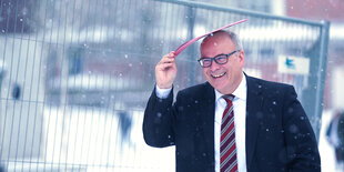 Ein Mann hält sich zum Schutz vor Schneeregen eine rote Mappe über den Kopf