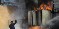 Ein Feuerwehrmann steht vor einem brennenden Kraftwerk.