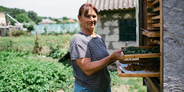 Aurica Bugniak steht in ihrem Gemüsegarten und zieht eine Schublade mit getrockneten Kräutern aus einem Trockenschrank