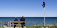 Zwei Personen sitzen an der Stohler Steilküste auf einer Bank und schauen auf die Ostsee.