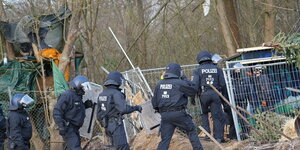 Polizisten gehen durch einen Zaun , im Hitnergrund ein Baumhaus