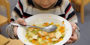 Ein Kind hält einen Teller mit Gemüsesuppe in der Hand.
