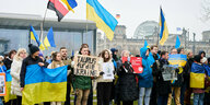 Menschen mit ukrainischen Flaggen und Schildern stehen zusammen vor dem Kanzleramt