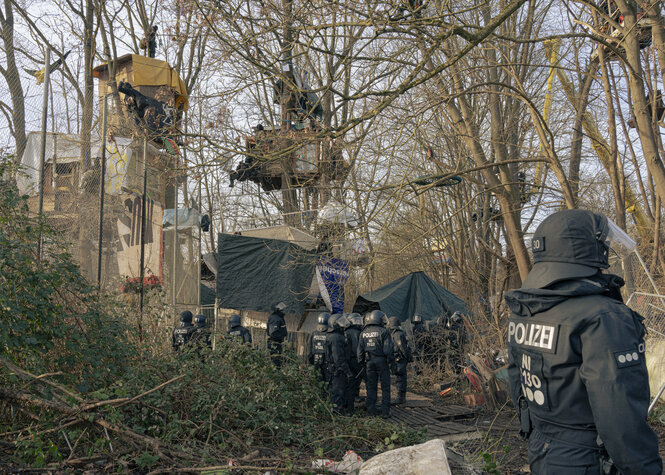 Polizisten stehen vor Baumhäusern in einem Wald.