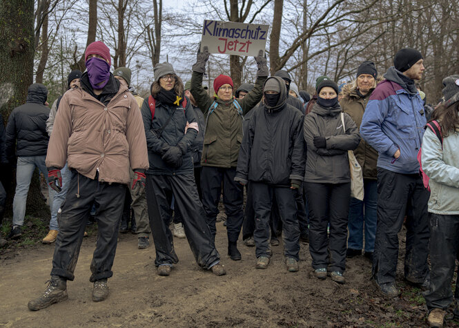 Menschen stehen nebeneinander, eine Frau hält ein Schild hoch mit der Aufschrift "Klimaschutz jetzt"