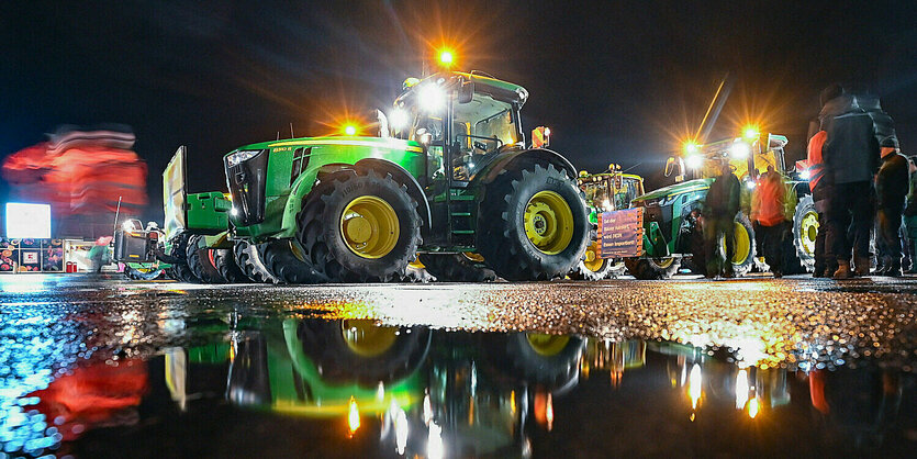 Viele Traktoren von Landwirten stehen auf einem Parkplatz und spiegeln sich in Pfützen.