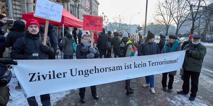 Demonstrant*innen halten ein Transparent und protestieren vor einem Gericht