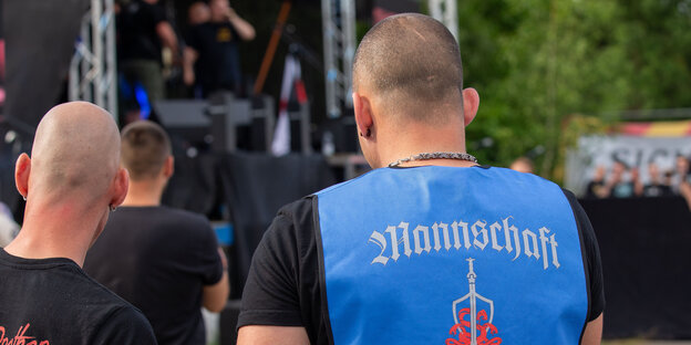 Zwei kahl geschorene Männer stehen bei dem Rechtsrockfestival Schild und Schwert vor einer Bühne.
