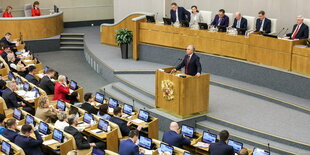 Stehender Redner am Pult spricht zu sitzenden Abgeordneten