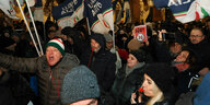 Menge weißer Menschen im Dunkeln mit Fahnen der Partei Fratelli d'Italia, Trillerpfeifen und einem Demoschild, auf dem ein Tempo-30-Symbol durchgestrichen ist