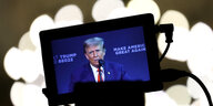 Donald Trump bei einer Wahlkampfverqnstaltung spricht in ein Mikrofon, zu sehen auf dem Bildschirm eines Smartphones