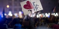 Demonstrant hält Papptafel hoch, auf der ein Herz ein Hakenkreuz zerschlägt