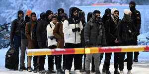 Migranten stehen im Schnee vor einer geschlossenen Schranke