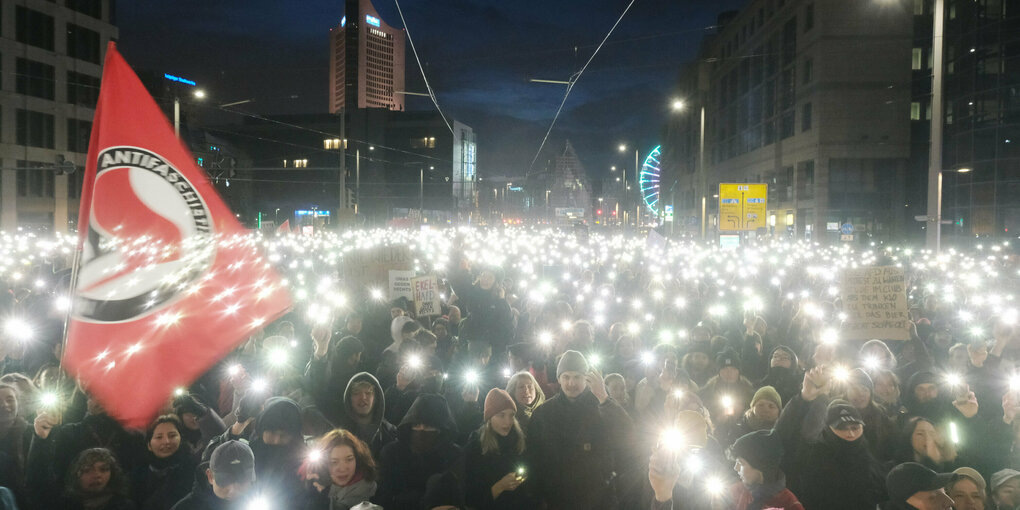 Aufnahme einer Lichterdemo gegen Faschismus am Abend. Ein Meer aus Lichtern füllt das Bild. Im linken Bildrand ist eine Antifa-Flagge zu erkennen.