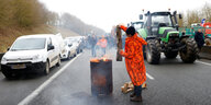 Ein protestierende Bauer in einem roten Mantel wirft Holz in ein brennendes Fass, während einer Blockader der Autobahn