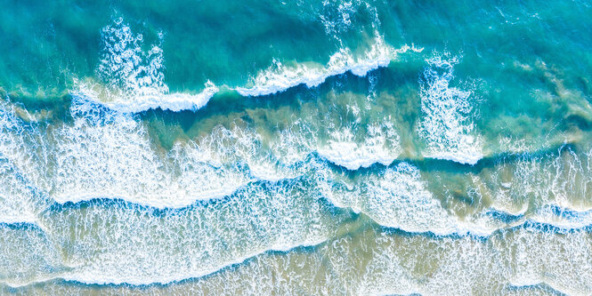 Die türkise Wasseroberfläche des Meeres und Brandung an einem Sandstrand