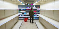 Eine Person mit Einkaufskorb zwischen leeren Supermarktregalen