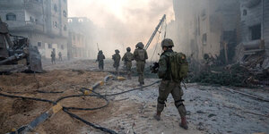 Eine Gruppe israelischer Soldaten geht durch eine zerstörte Straße, die von Ruinen gesäumt wird