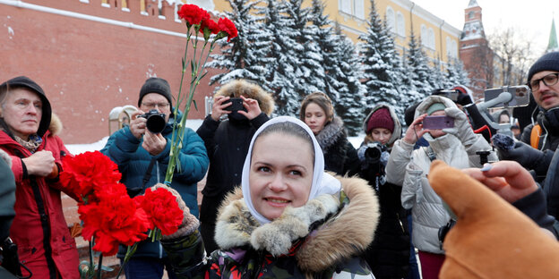 Maria Andrejewa steht in einer sie fotografierenden Menschenmenge und hält rote Rosen in die Luft