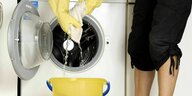 Eine Person mit Gummihandschuhen nimmt mit einem Lappen das ausgelaufene Wasser ihrer Waschmaschine auf