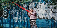 Pisitakun Kuantalaeng steht vor einem Zaun mit Graffiti und bläst in die Khaen