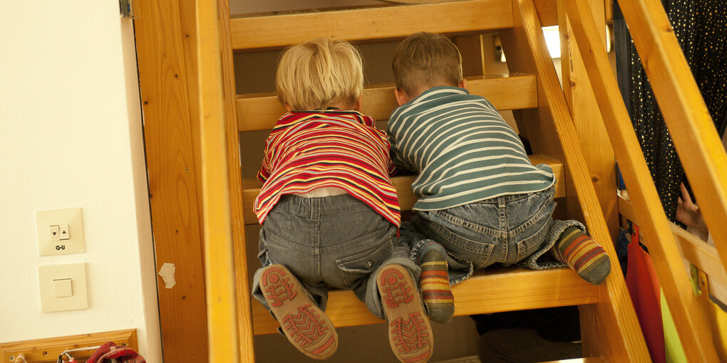 Zwei Kinder hocken auf einer Leiter und gucken durch die Stufen