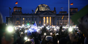 Eine Menschenmenge hält bei Nacht ihre Taschenlampenlichter hoch. Sie stehen vor dem Reichstag.