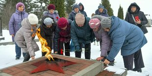 Frauen stehen an einem Denkmal mit rotem Sowjetstern und einer Flamme und legen Blumen ab