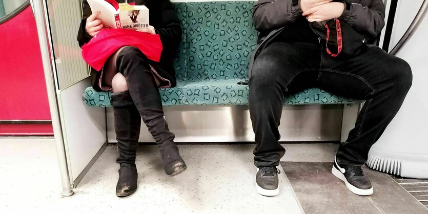 Eine Frau mit übergeschlagenen Beinen sitzt neben einem raumgreifenden Mann in der UBahn