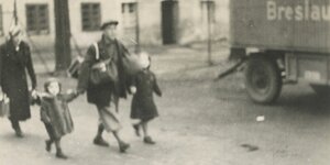 Eine alte Schwarz-Weiß-Aufnahme von zwei Erwachsenen und zwei Kindern. Die Erwachsenen tragen Gepäck