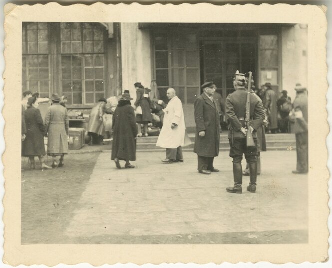 Eine alte Schwarz-Weiß-Aufnahme von einer Gruppe von Menschen, einer trägt ein Gewehr auf dem Rücken