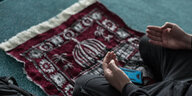Ein Mensch sitzt auf einem Teppich und betet.