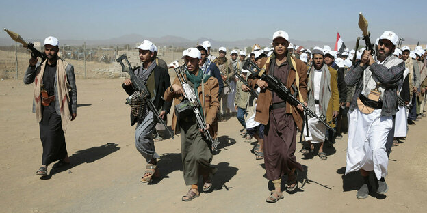 Huthi-Kämpfer laufen über einen trockenen Sandweg.