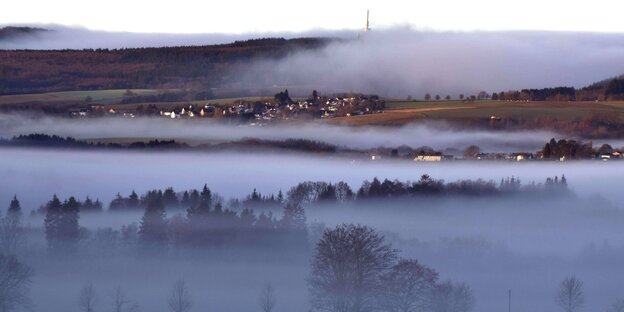 Hunsrücker Landschaft mit Dörfern, Wald und Wiesen am Rand des Nationalparks Hunsrück-Hochwald mit Nebel an einem frühen Wintermorgen