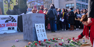 Ein Betonsockel ragt aus dem Boden, um den Sockel herum sind rote Kerzen und Blumen auf das Mahnmal für die Opfer von Rassismus und Polizeigewalt gestreut.