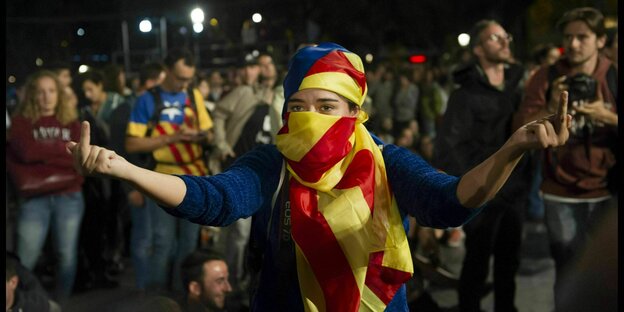 Tag des Referendums in Barcelona, eine junge Frau, die ihr Gesicht mit der katalonischen Flagge verhüllt, zeigt den Stinkefinger