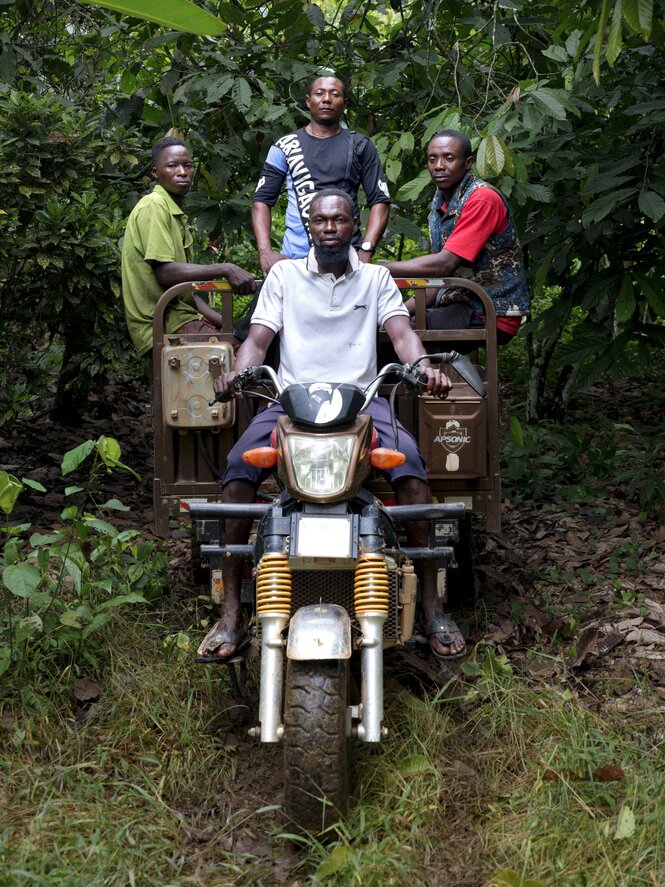 Ein Mann transportiert drei Männer auf der Ladefläche seines Mopeds im Wald