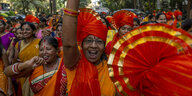 Frauen in traditioneller Kleidung in orange-gelben Tönen und großen Schirmen feiern und lachen ausgelassen auf der Straße