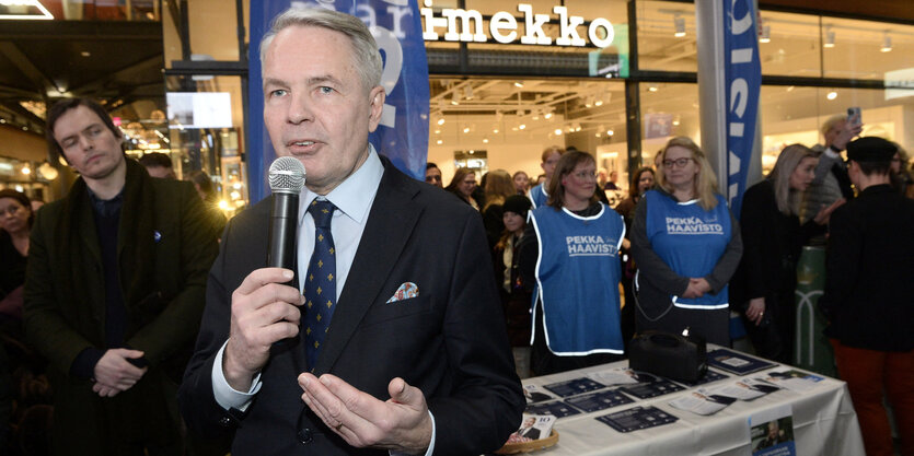 Mann mit einem Mikrofon, im Hintergrund Wahlkampfhelfer*innen