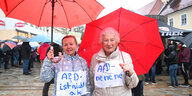 Zwei alte Frauen mit roten Regenschirmen und Protestplakaten gegen die AfD