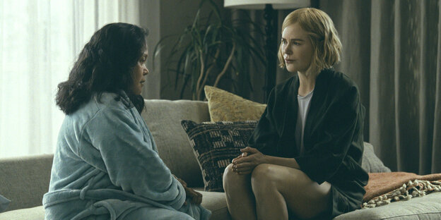 Eine Frau - Nicole Kidman - sitzt mit einer anderen Frau, die einen Bademantel trägt, auf einem Sofa
