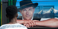 Ein Mann schaut auf eine vorbeifahrende Straßenbahn mit Werbeplakat.