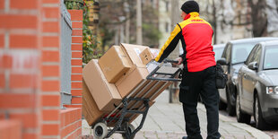 Ein Paketbote mit einer Sackkarre, auf der Pakete gestapelt sind