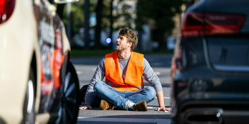 Ein Klimaaktivist sitzt in Warnweste auf der Straße und blockiert sie.