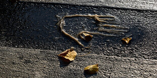 Klebespuren auf Asphalt: ein Handabdruck und Herbstblätter auf einer Straße