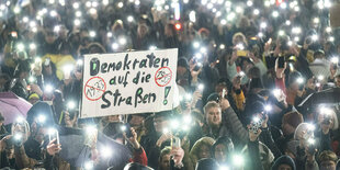 Menschen protestieren mit ihren Taschenlampen am Smartphone gegen die AfD - in der Mitte der Menge ein Schild: Demokraten auf die Straßen