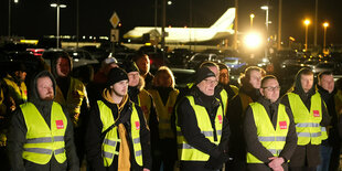 Eine Gruppe von Menschen bei einer Versammlung, im Hintergrund ein Flugzeug.