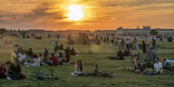 Menschen sitzen während des Sonnenuntergangs auf einer Wiese am Tempelhofer Feld, in der Ferne ist das Flughafengebäude zu sehen